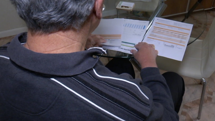 An elderly man looks at his bills on a glass table