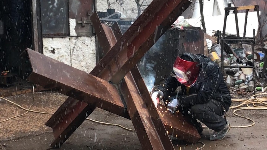 a man squats down and welds a large metal object 