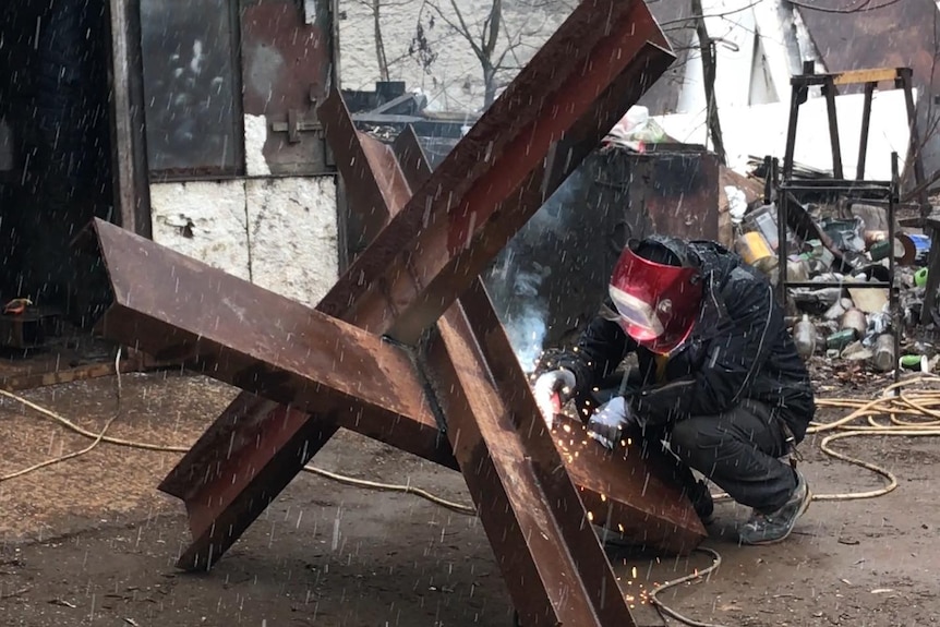 a man squats down and welds a large metal object 
