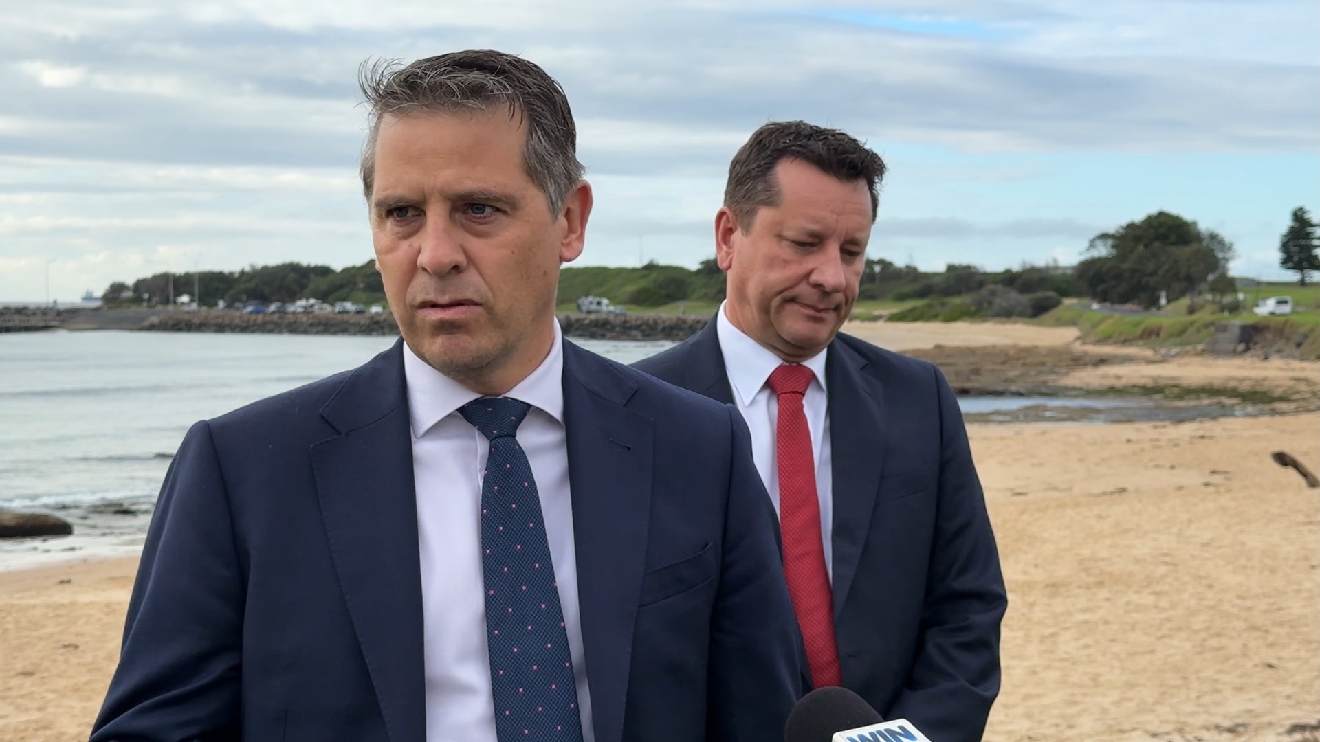 Ryan Park in suit and Paul Scully in suit look concerned on a beach