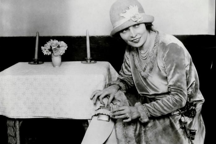 A prohibition-era archival photograph of a woman hiding a flask of alcohol in her stocking