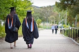 Two women walk through university grounds in graduation robes