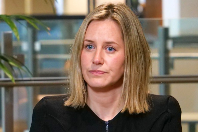 A blond woman wearing a dark jacket listening during an interview.