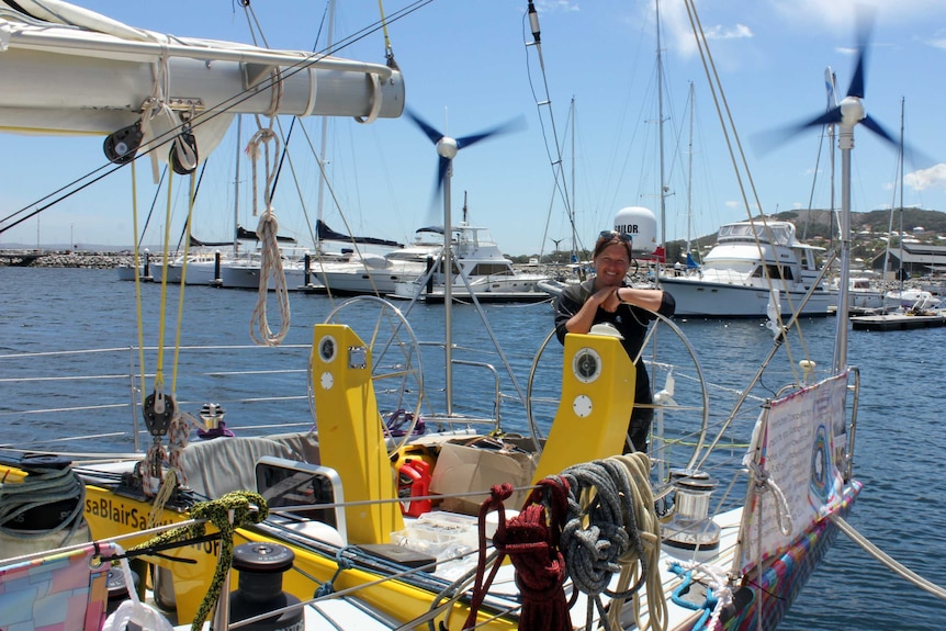 A woman stands at the helm of a yacht moored in a marina.