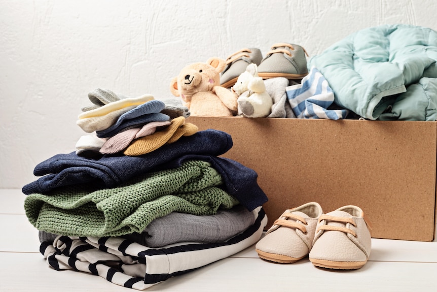 A neat pile of childrens' clothes, including a teddy bear and little shoes, in a cardboard box