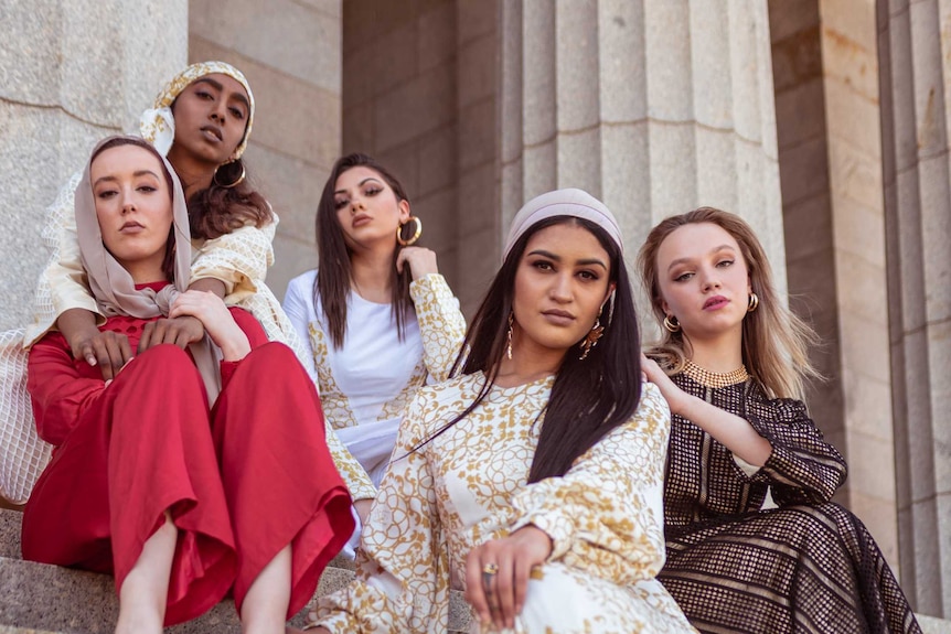 Five "modest" fashion models sit together on some steps.