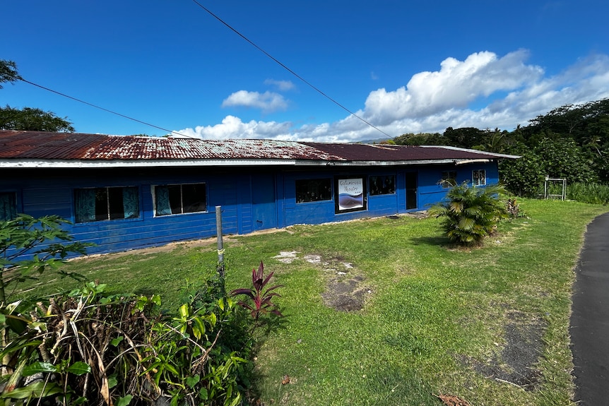 A low-set blue building with a rusty corrugated iron roof.