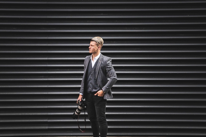 Josh Brnjac stands on the street holding a camera.