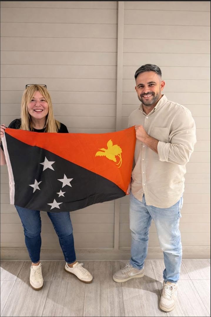 A man and woman hold a red, black, white and yellow PNG flag.