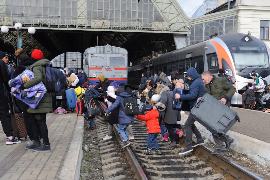 A group of children with some adults run across train tracks at a station