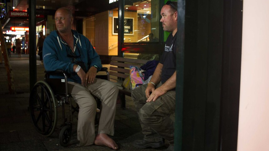 Brian Willcox sits with a homeless man at a bus stop in Perth CBD