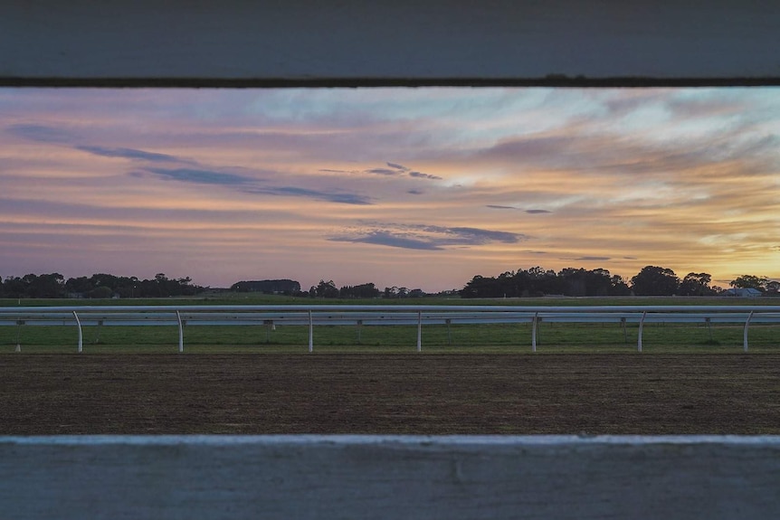 The sun rises over a quiet dirt race track, spreading colours of pastel blue, pink and orange.
