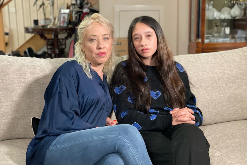 Stieve and Trinity De Lance sit on a couch inside their home and look sad.