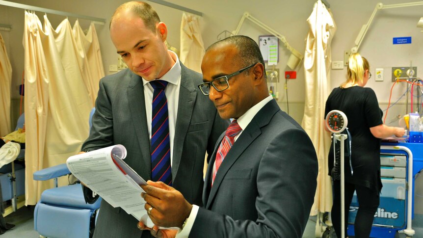 Two men in suits stand in a hospital