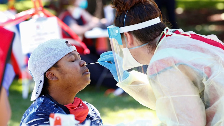 A woman closes her eyes while a health worker in full PPE sticks a swab in her nostril