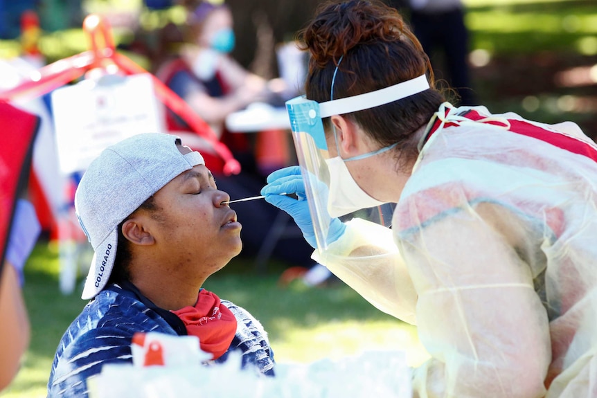 A woman closes her eyes while a health worker in full PPE sticks a swab in her nostril