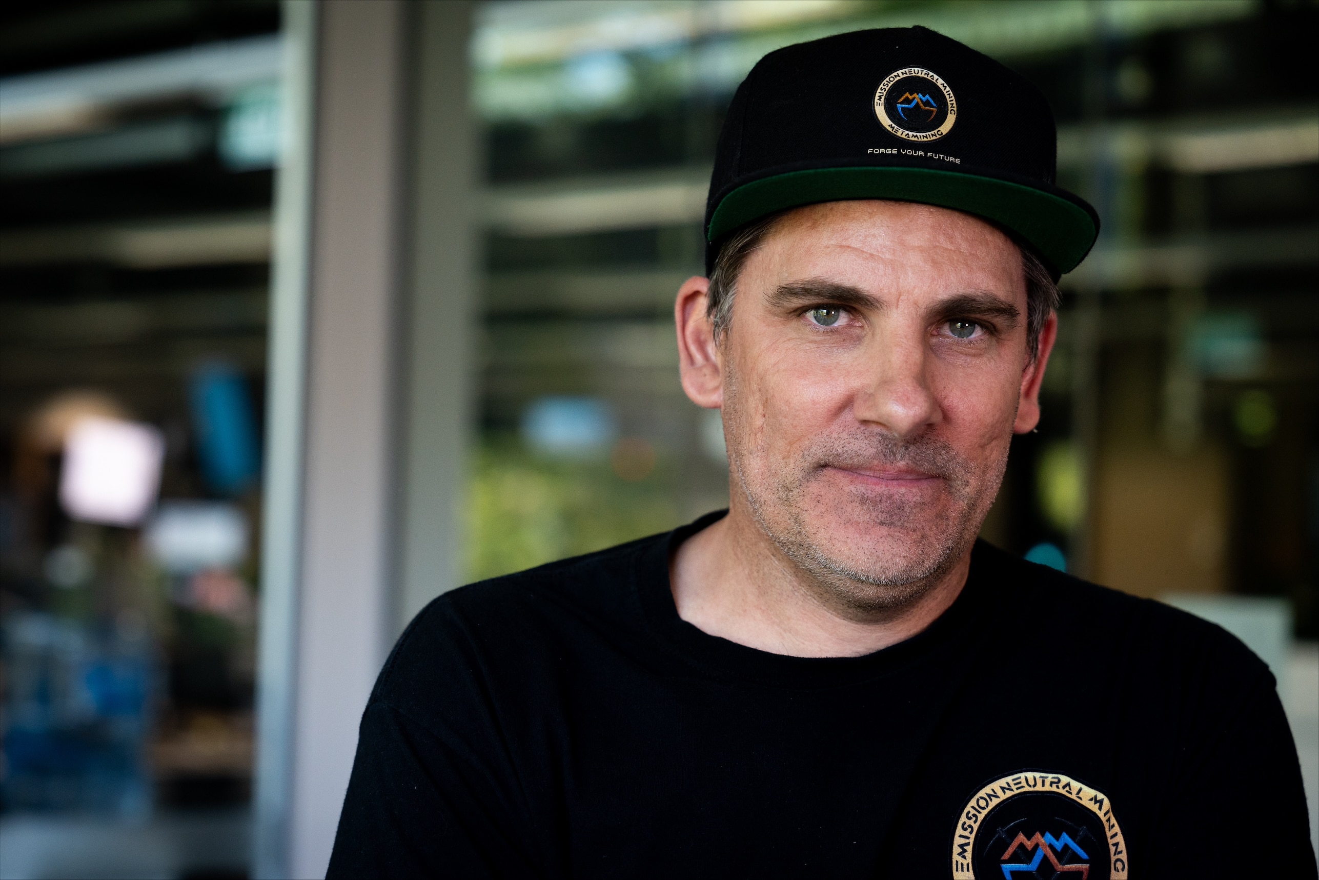 A man wearing a black tshirt and black cap in an office.