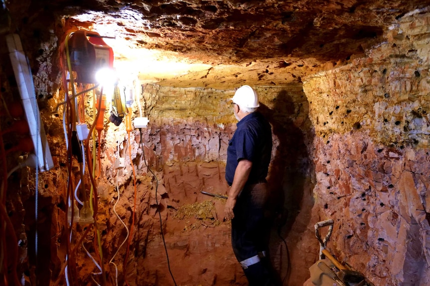 Paul Hunton stands looking away from the camera towards a wall of red rock in an underground mine.