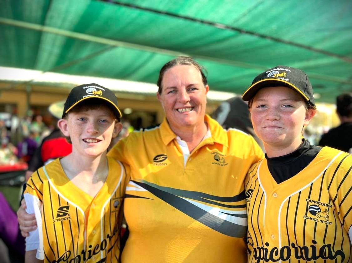 A young boy and girl wearing a yellow shirt and black hat standing with their mum also wearing a yellow and black shirt.