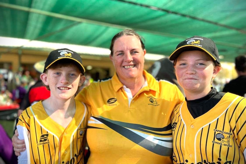 A young boy and girl wearing a yellow shirt and black hat standing with their mum also wearing a yellow and black shirt.