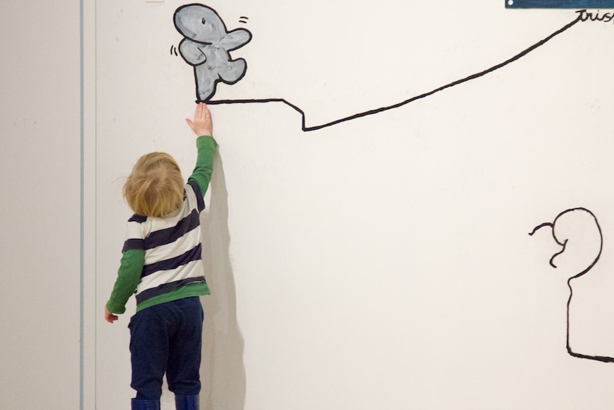 A small child reaches up to touch a line painted on a wall.