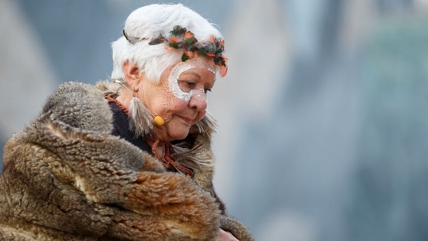 Aunty Fay Carter wearing an Indigenous fur cloak with white markings on her face. 