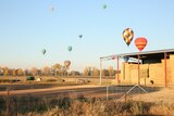 A rural property with hot air balloons dotting the sky above it.