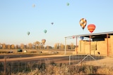 A rural property with hot air balloons dotting the sky above it.