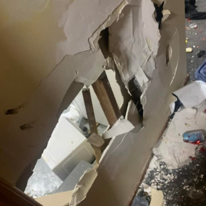 A large hole in the wall in a social housing unit, plaster littered across the floor with other trash