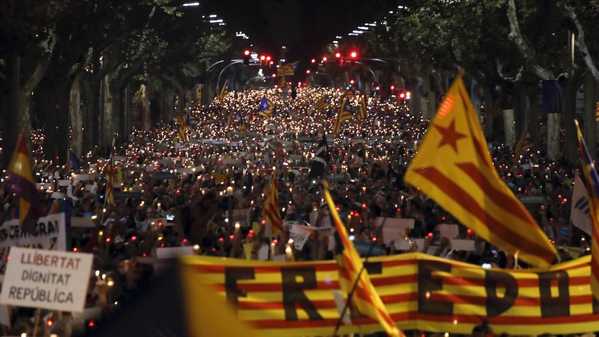 Thousands of people holding candles gather on a street in Barcelona at night.