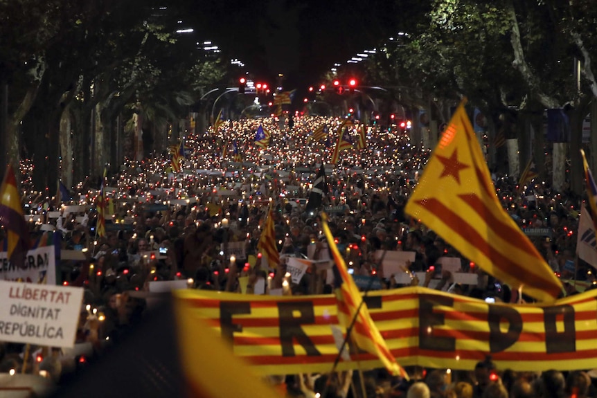 Thousands of people holding candles gather on a street in Barcelona at night.