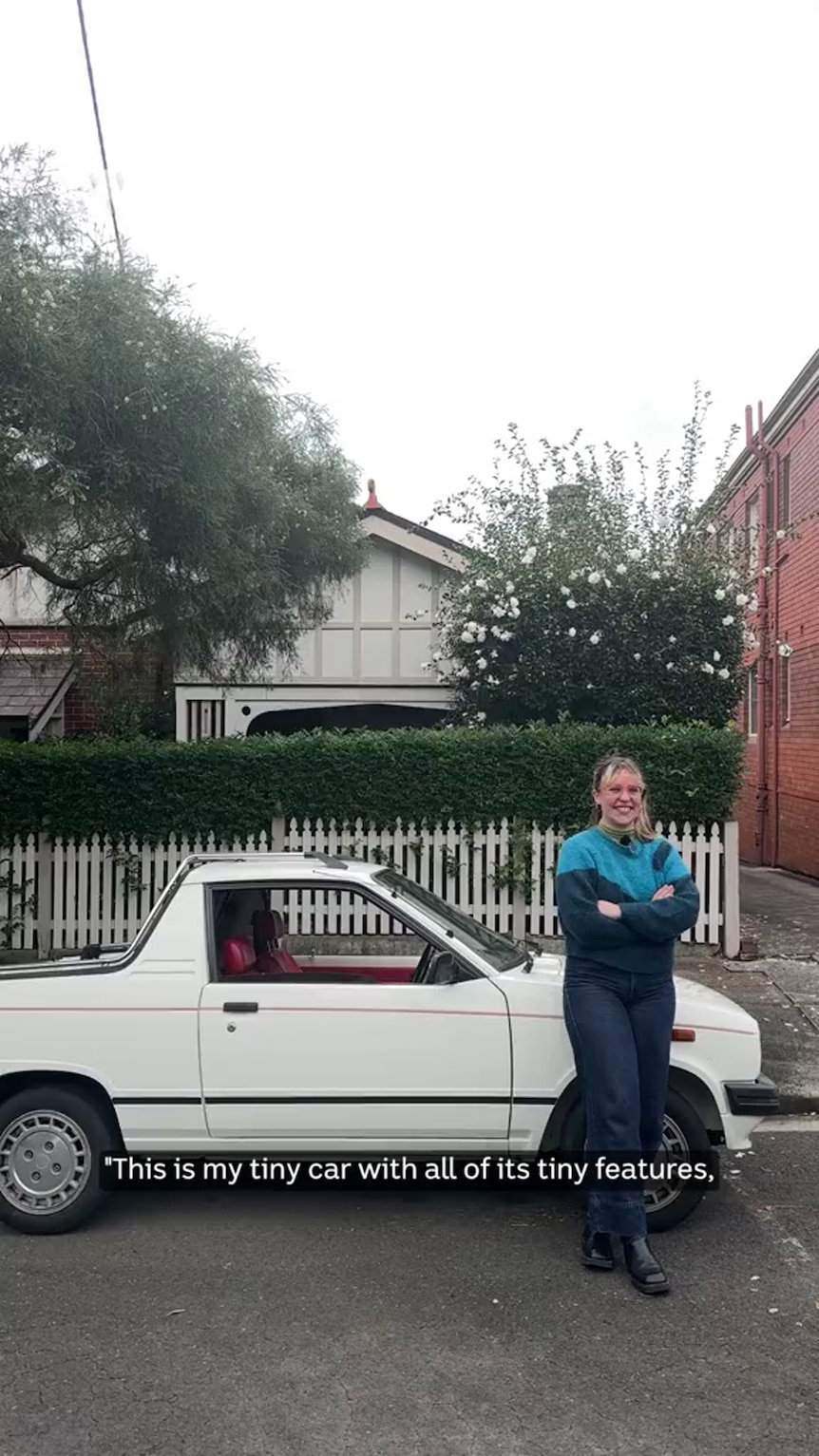 A young woman with light tone skin and dressed in jeans and jumper stands before a small ute parked on a suburban street