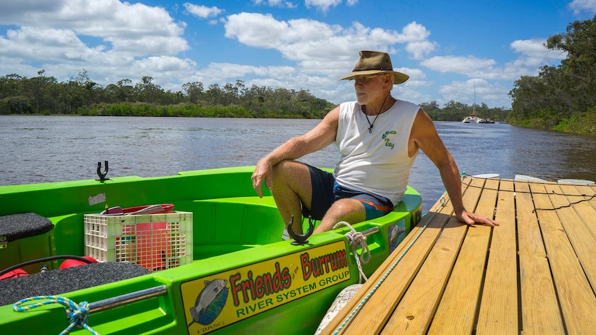 President of Friends of the Burrum River System Tim Thornton sits on a pontoon beside a small boat, looking out over the river.