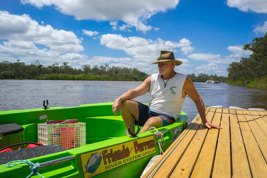 President of Friends of the Burrum River System Tim Thornton sits on a pontoon beside a small boat, looking out over the river.