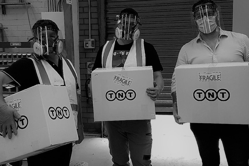 Three men holding boxes wearing face shields.