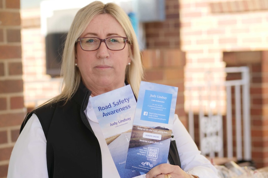 A lady with blonde hair hold up two brochures with the words "road safety awareness" on it.