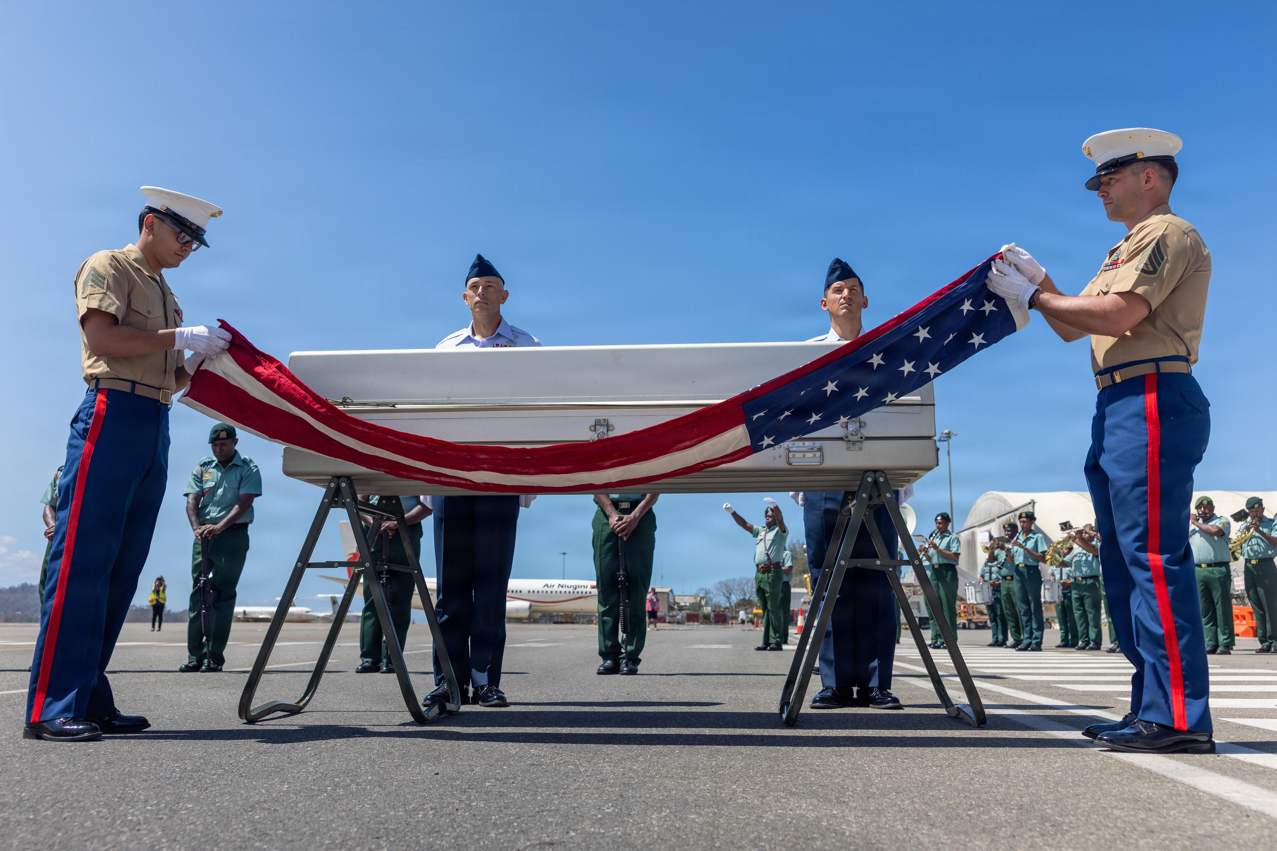US military personnel unveil a flag over a coffin on an outside air strip.