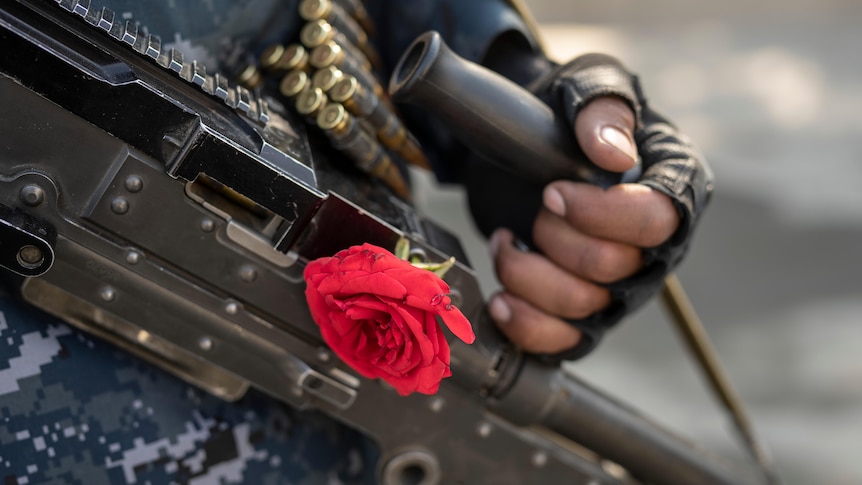 A man holds a gun with a red rose on it