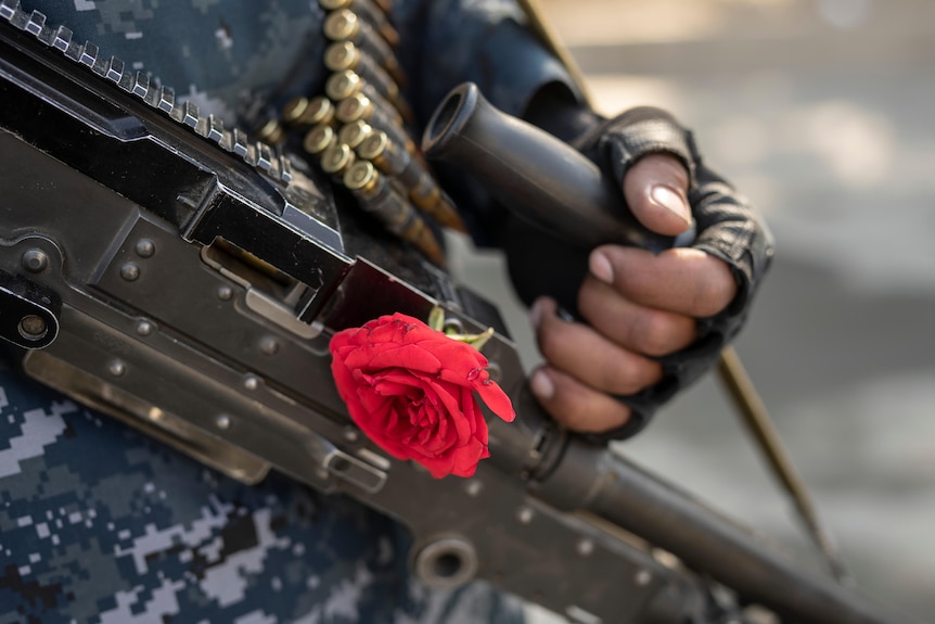 A man holds a gun with a red rose on it