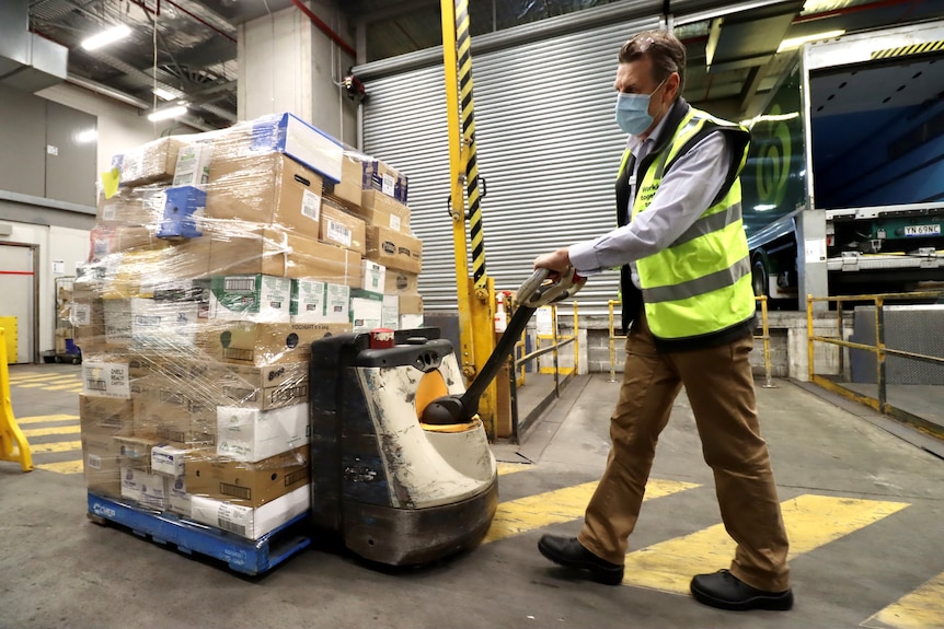 A man in high-vis vest and mask moves a pallet loaded with boxes.