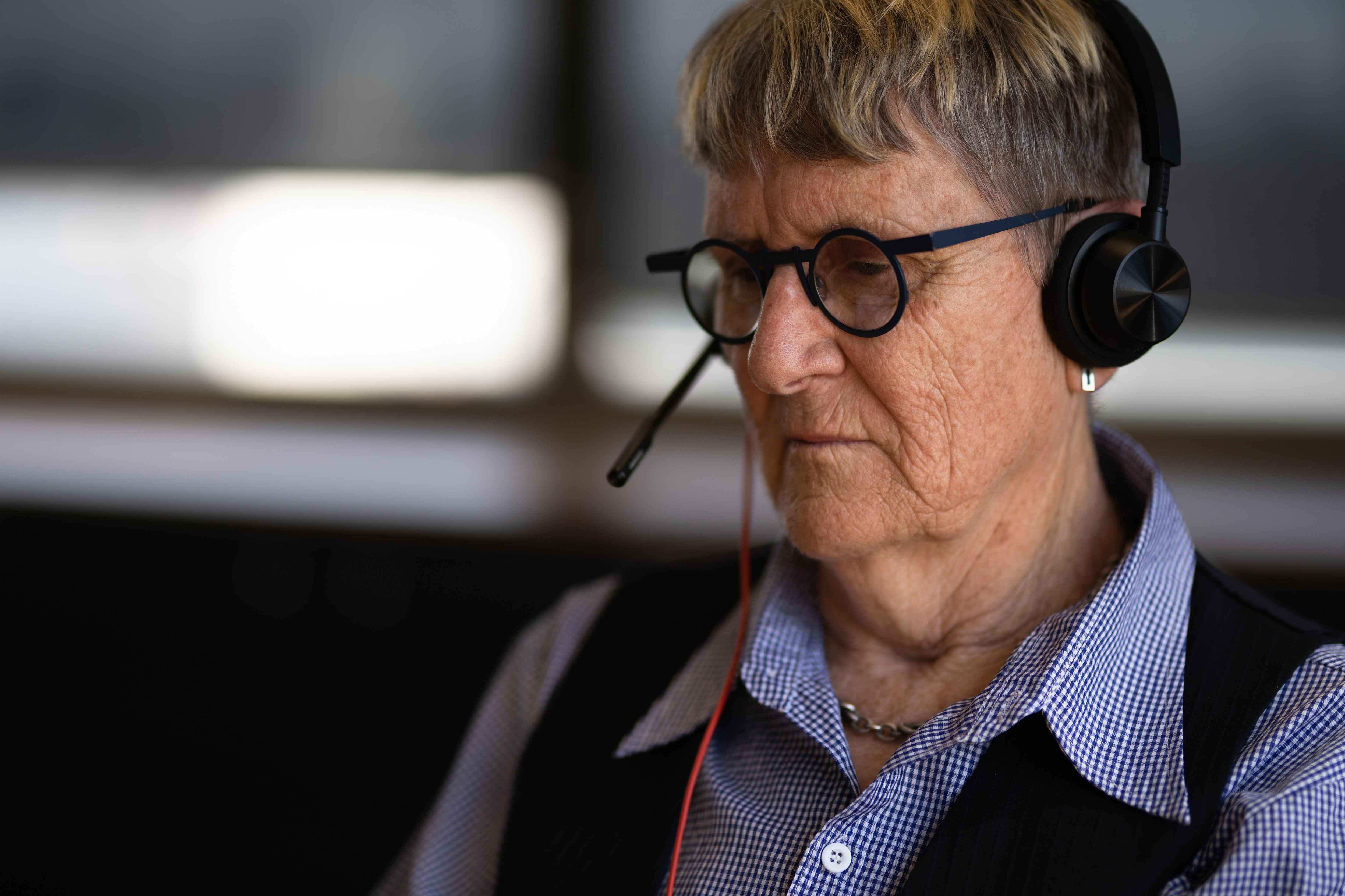 Woman with black glasses and a blue shirt taking a call with headphones.