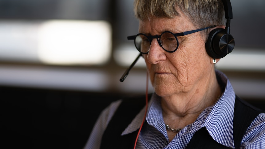 Woman with black glasses and a blue shirt taking a call with headphones.