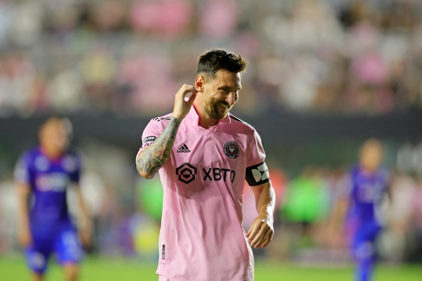 A man in a pink top smiling on a soccer pitch 