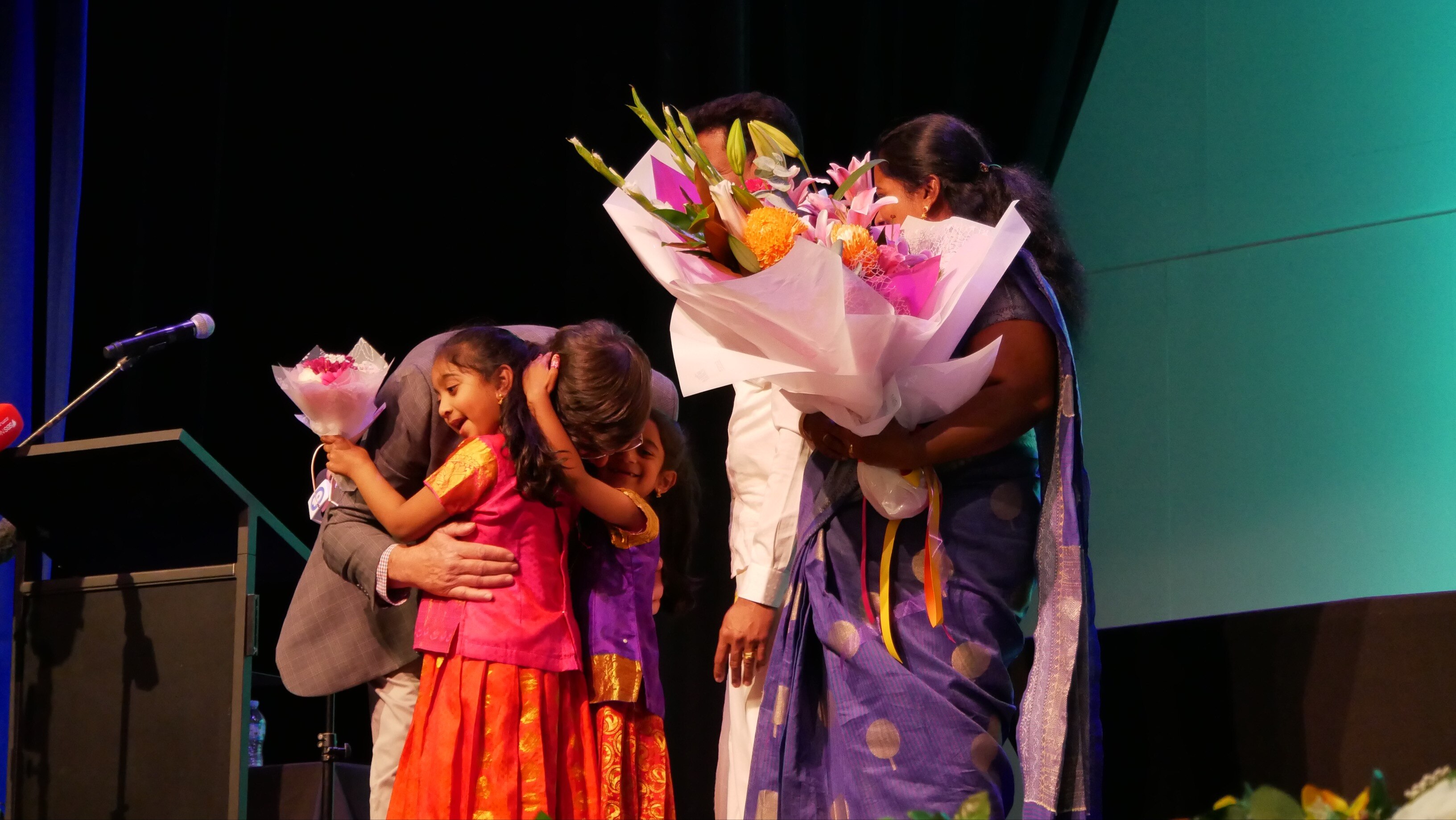 A man hugs two girls as their parents watch on. 