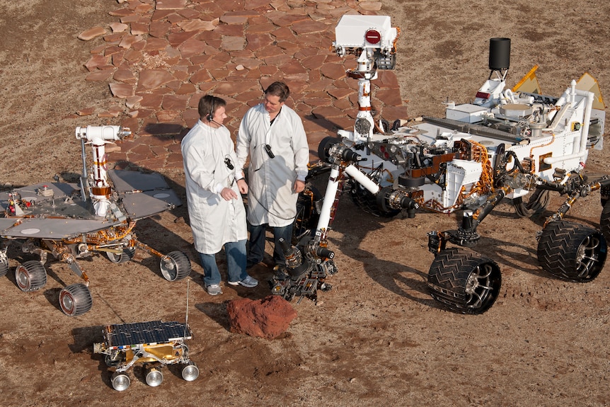 Engineers stand with three generations of Mars rovers