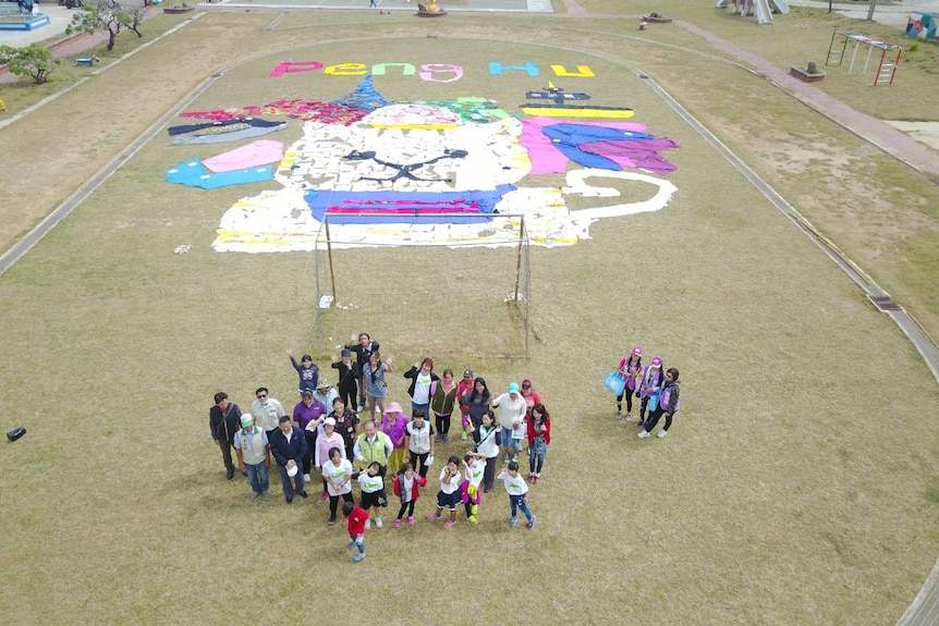 Staff, students and artists at Hujing Elementary School with a newly created cat mural using recycled materials.