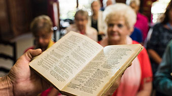 Pages of bible open, with older women in background.
