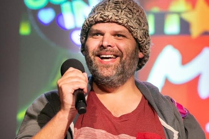 A man wearing a beanie laughs as he talks into a mic