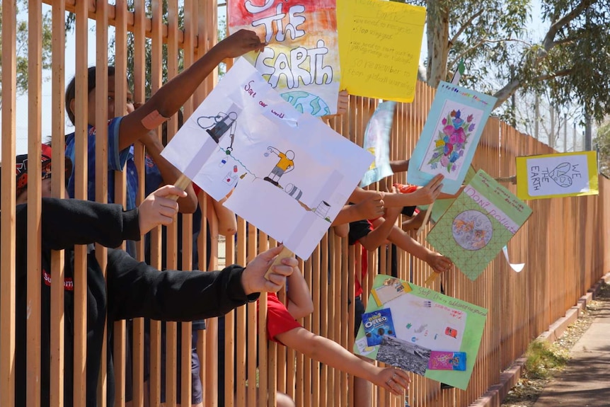 Students in Tennant Creek wave signs at passing cars through the schoolyard fence.