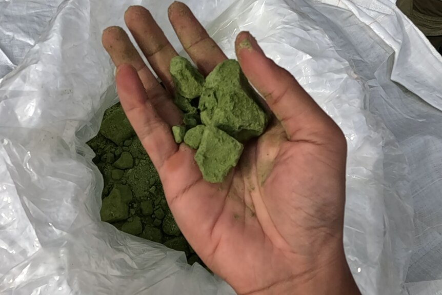 A green rock substance in the palm of a hand.